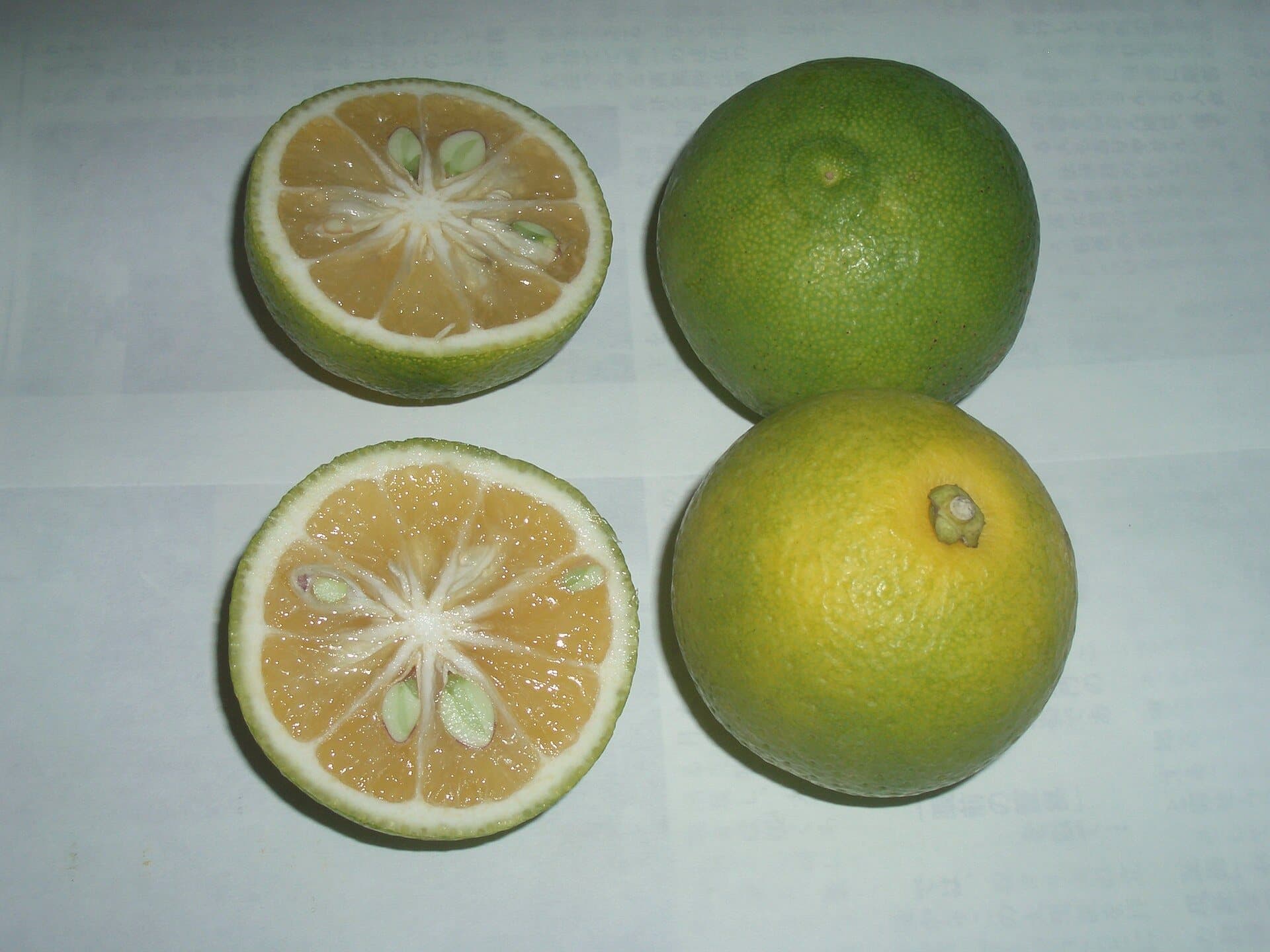 Kabosu halved to show juicy flesh, next to whole fruits turning yellow